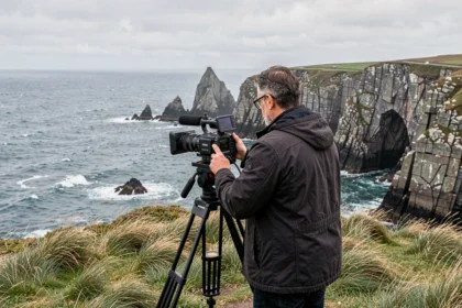Vidéaste professionnel filmant le paysage côtier breton depuis une falaise de granit